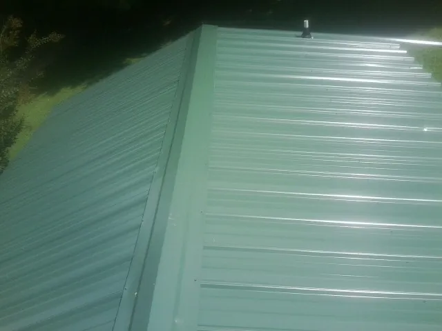 New green metal panels meeting at the ridge of a roof — Flat Roof Repair work by our crew in Baker