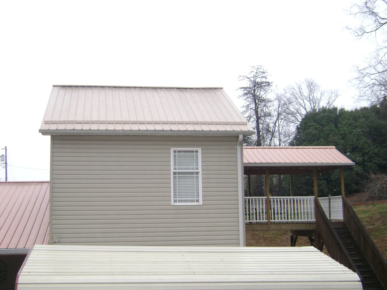 Tan metal roofs on a two story addition and attached porch, from a Roof Replacement job in Baker